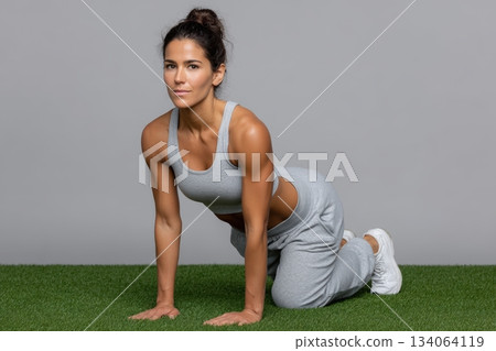 Fitness coach demonstrates effective hip stretch on a grassy surface indoors 134064119