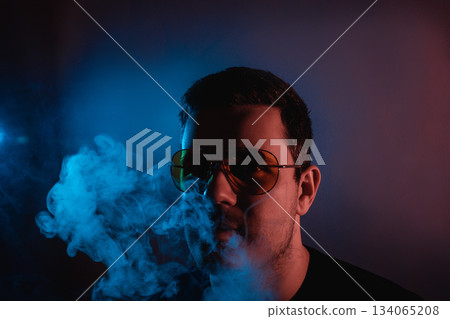 Man in neon light enjoying hookah smoke at a vibrant evening lounge atmosphere 134065208