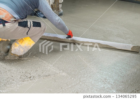 Construction Worker Smoothing Concrete Floor with Level Tool for Durable Surface Creation 134065295