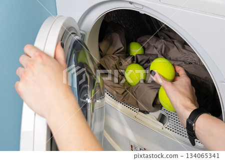 Woman Putting Tennis Balls into Clothes Dryer with Jacket for Fluffing and Wrinkle Reduction Woman Putting Tennis Balls into Clothes Dryer with Jacket for Fluffing and Wrinkle Reduction 134065341