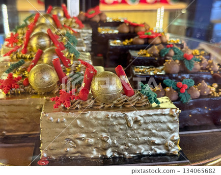 Golden Christmas pastries cake topped with chocolate decorations and festive holly details. Holiday indulgence, elegant bakery display, seasonal sweets and luxurious winter celebration mood Golden Christmas pastries cake topped with chocolate decorations and festive holly details. Holiday indulgence, elegant bakery display, seasonal sweets and luxurious winter celebration mood 134065682
