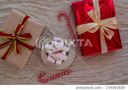Flat-lay top view of a festive Christmas arrangement featuring a mug filled with marshmallows, red-and-white candy canes, and holiday gift boxes. Cozy winter still life perfect for seasonal promotions 134065689