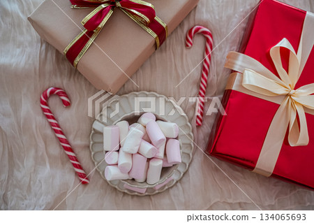 Flat-lay top view of a holiday mug filled with marshmallows surrounded by wrapped Christmas presents. Cozy festive arrangement ideal for greeting cards, social media, seasonal marketing, and holiday 134065693