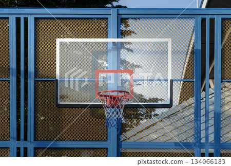 A basketball hoop, featuring an orange metal rim and net mounted on a Fiberglass Basketball Backboard. A basketball hoop, featuring an orange metal rim and net mounted on a Fiberglass Basketball Backboard. 134066183