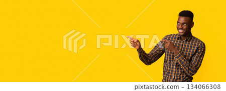 Look There. Cheerful African American Guy Pointing Aside At Copy Space Over Yellow Background With Two Fingers, Positive Black Male Showing Free Place For Your Design Or Advertisement, Panorama Look There. Cheerful African American Guy Pointing Aside At Copy Space Over Yellow Background With Two Fingers, Positive Black Male Showing Free Place For Your Design Or Advertisement, Panorama 134066308