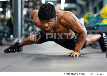 Push-up, press-up at gym concept. Motivated black guy bodybuilder doing some push-ups with one hand gym, panorama with copy space. African american shirtless muscular man working on triceps, biceps Push-up, press-up at gym concept. Motivated black guy bodybuilder doing some push-ups with one hand gym, panorama with copy space. African american shirtless muscular man working on triceps, biceps 134066322