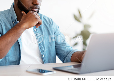Busy Black Entrepreneur Working With Laptop At Office, Unrecognizable African Businessman Sitting At Desk, Looking At Computer Screen And Touching Chin, Closeup Shot, Cropped Image 134066346