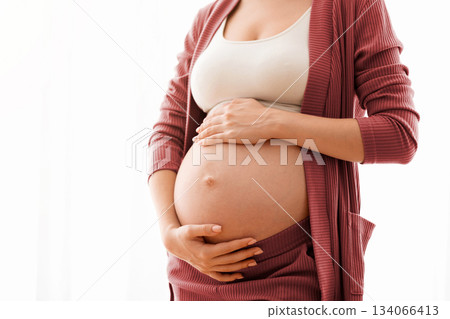 Unrecognizable Pregnant Lady Touching Her Naked Belly, Closeup Shot. Expectant Mother Standing Against Window At Home And Tenderly Embracing Tummy, Enjoying Pregnancy Time, Cropped Image, Copy Space 134066413