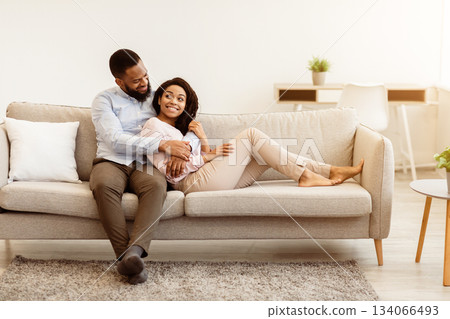 Happy Loving Family. Beautiful african american couple spending weekend together, resting on the couch indoors at home in living room, relaxing and enjoying the company of each other, hugging Happy Loving Family. Beautiful african american couple spending weekend together, resting on the couch indoors at home in living room, relaxing and enjoying the company of each other, hugging 134066493