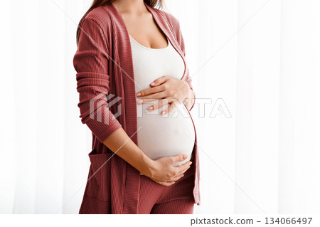 Portrait Of Joyful Pregnant Woman Embracing Her Belly While Standing Near Window At Home, Happy Expectant Mother Enjoying Healthy Pregnancy And Prenanal Time, Touching Tummy And Smiling, Copy Space 134066497