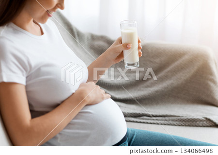 Cropped Shot Of Young Pregnant Woman Holding Glass With Milk And Touching Tummy While Resting On Comfortable Couch At Home, Expectant Lady Enjoying Healthy Calcium Drink, Closeup Image, Side View Cropped Shot Of Young Pregnant Woman Holding Glass With Milk And Touching Tummy While Resting On Comfortable Couch At Home, Expectant Lady Enjoying Healthy Calcium Drink, Closeup Image, Side View 134066498