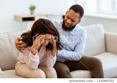 Problems And Moral Support. Loving african american man soothing and comforting his crying stressed woman, apologizing after quarrel, boyfriend hugging girlfriend shoulder, sitting on couch 134066502