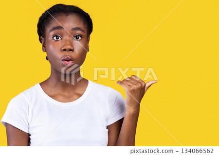 Shocked African American Lady Pointing Thumb Aside At Copy Space Advertising Your Text Posing Standing On Yellow Background, Studio Shot. Look There Concept. Panorama 134066562