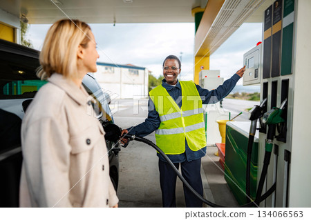 Attendant serving customer refilling car at gas station 134066563