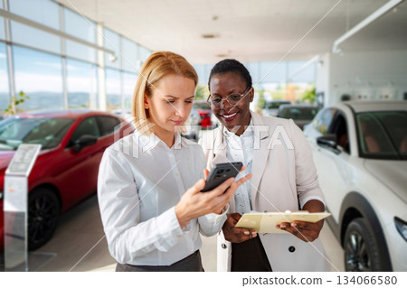 Salesperson and customer using phone in car dealership 134066580