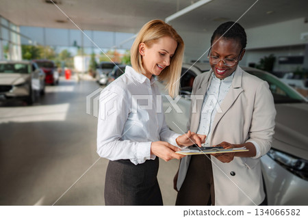 Women discussing car purchase paperwork in dealership showroom 134066582