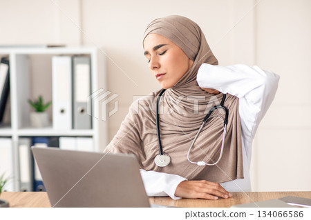Exhausted muslim woman in hijab doctor rubbing her neck while working with laptop in her cabinet in clinic, copy space. Tired lady physician suffering from office syndrome, overworked doctors concept Exhausted muslim woman in hijab doctor rubbing her neck while working with laptop in her cabinet in clinic, copy space. Tired lady physician suffering from office syndrome, overworked doctors concept 134066586