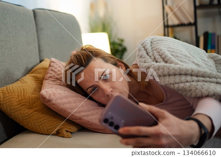 Woman experiencing insomnia doomscrolling phone in bed at night 134066610