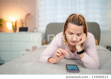 Woman lying on bed using smartphone at home Woman lying on bed using smartphone at home 134066615