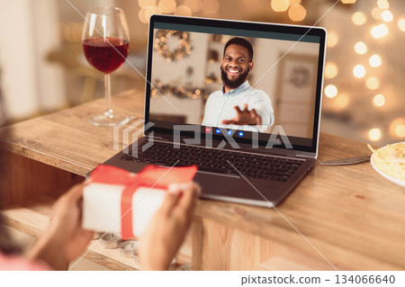 Long Distance Relationship. African american couple having online virtual date, man reaching hand to webcam in videochat with videoconferencing app window, woman showing him present box 134066640