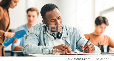 Knowledge Concept. Portrait of serious African American male student sitting at desk in classroom at university, writing in notebook, taking notes, exam or test. Return to college and high school 134066642