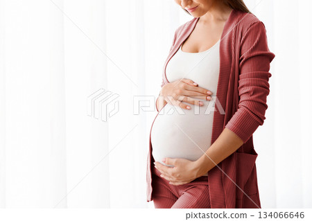Expecting A Baby. Portrait Of Happy Young Pregnant Lady Tenderly Touching Belly Near Window At Home, Beautiful Millennial Awaiting Mother Embracing Her Tummy And Smiling, Enjoying Pregnancy Time 134066646