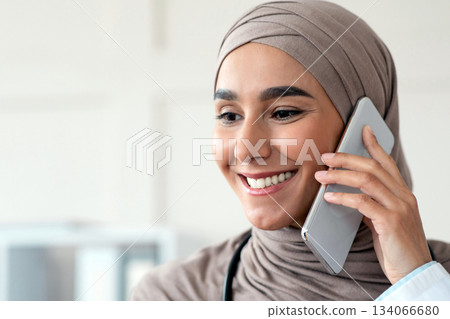 Closeup portrait of cheerful female doctor muslim woman talking on mobile phone and looking at copy space. Smiling young lady in hijab having conversation with patient on smartphone Closeup portrait of cheerful female doctor muslim woman talking on mobile phone and looking at copy space. Smiling young lady in hijab having conversation with patient on smartphone 134066680