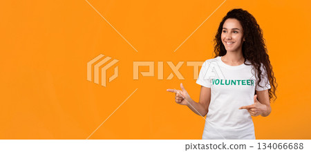 Look There. Female Volunteer Pointing Fingers Aside Showing Copy Space Standing Over Yellow Studio Background. Activist Advertising Volunteering Event Or Offer. Panorama 134066688