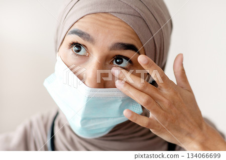 Avoid face touching, Coronavirus prevention, Doctors protection during COVID-19 pandemic. Overworked female doctor in protective face mask and hijab touching her eyes, closeup portrait 134066699
