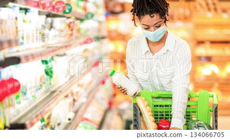 Supermarket Shopping Concept. African American Woman Buying Food Grocery Standing With Pushcart Near Store Shelf Indoors, Wearing Face Mask. Consumerism, Female Customer In Market Shop. Free Space 134066705