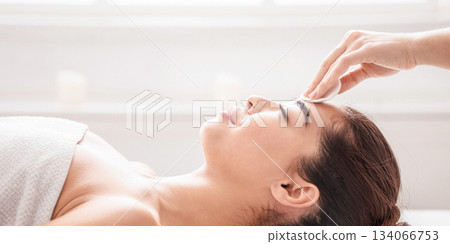 Facial Treatment. Professional Cosmetologist Cleansing Skin Of Young Asian Woman Before Beauty Procedures, Using Cotton Pad, Relaxed Korean Female Lying On Massage Table With Closed Eyes, Side View 134066753