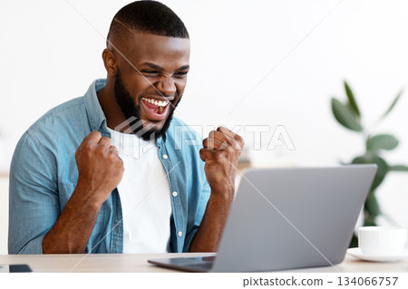 Joyful Black Guy With Laptop Celebrating Business Success At Workplace In Modern Office, African Entrepreneur Looking At Computer Screen, Raising Fists And Exclaiming With Excitement, Free Space Joyful Black Guy With Laptop Celebrating Business Success At Workplace In Modern Office, African Entrepreneur Looking At Computer Screen, Raising Fists And Exclaiming With Excitement, Free Space 134066757