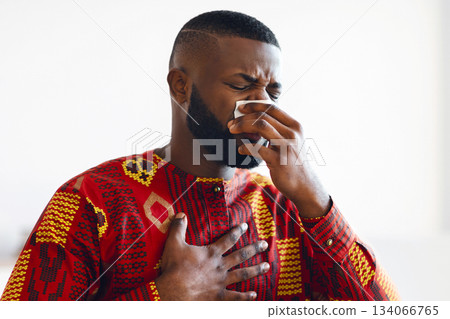 Coronavirus Symptoms. Black Freelancer Guy In Ethnic Costume Feeling Sick And Unwell At Home, Ill African American Man Suffering Runny Nose, Sitting At Desk With Laptop Computer, Copy Space 134066765