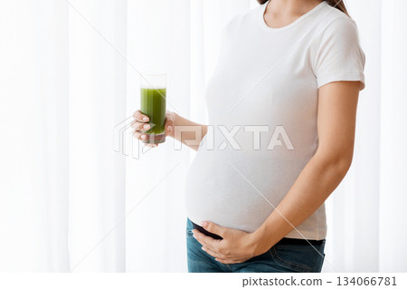 Prenanal Vitamins. Portrait Of Happy Young Expectant Woman Holding Glass With Green Vegetable Smoothie While Standing Near Window At Home, Beautiful Pregnant Lady Enjoying Vitamin Drink, Copy Space Prenanal Vitamins. Portrait Of Happy Young Expectant Woman Holding Glass With Green Vegetable Smoothie While Standing Near Window At Home, Beautiful Pregnant Lady Enjoying Vitamin Drink, Copy Space 134066781