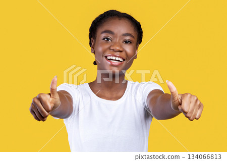 I Like It. Smiling African Woman Gesturing Thumbs Up With Both Hands Smiling To Camera Posing On Yellow Studio Background. Young Black Lady Showing Thumbs Approving And Advertising Something 134066813