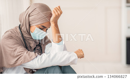 Sad arab woman doctor having difficult day at clinic, wearing protective face mask, sitting next to wall in her office and resting, empty space. Upset female doctor in hijab feeling exhausted Sad arab woman doctor having difficult day at clinic, wearing protective face mask, sitting next to wall in her office and resting, empty space. Upset female doctor in hijab feeling exhausted 134066827