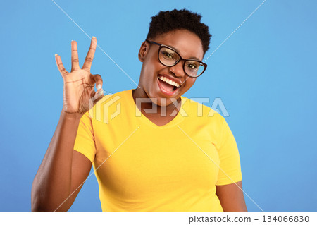 Cheerful African Plus-Size Woman Gesturing Okay Sign Posing Standing Over Blue Studio Background, Smiling To Camera. I Am OK. Black Lady Approving Something Wearing Eyeglasses Cheerful African Plus-Size Woman Gesturing Okay Sign Posing Standing Over Blue Studio Background, Smiling To Camera. I Am OK. Black Lady Approving Something Wearing Eyeglasses 134066830