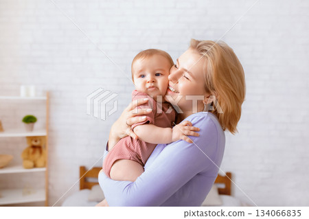 Happy loving mother blonde woman holding and kissing sweet little baby girl, young mom and adorable kid baby boy bonding, home interior, copy space. Motherhood, mom's love concept 134066835