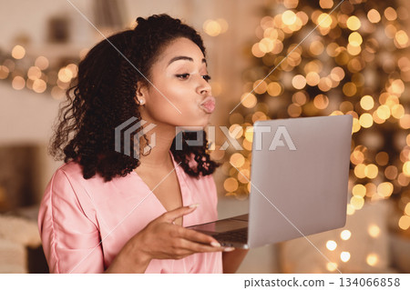 Virtual Or Long Distance Relationship And Online Dating. Portrait of beautiful young curly black woman holding laptop computer in hands and sending kisses to web camera during video chat with partner 134066858