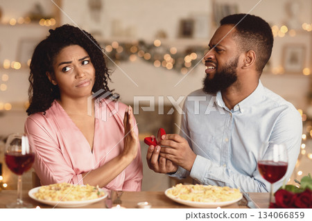 Proposal Fail. Portrait of unhappy african american man proposing to his gilfriend, holding open box with marriage ring, uninterested bored woman saying no, showing stop gesture with palm Proposal Fail. Portrait of unhappy african american man proposing to his gilfriend, holding open box with marriage ring, uninterested bored woman saying no, showing stop gesture with palm 134066859