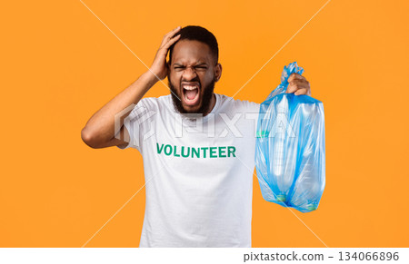 Mad African American Volunteer Man Shouting Holding Plastic Garbage Bag Full Of Litter Expressing Anger And Rage Standing Over Yellow Studio Background. Waste Sorting And Ecology Problems 134066896