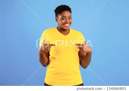 Choose Me. Cheerful Oversized African Lady Pointing Fingers At Herself Smiling To Camera Standing Posing Over Blue Background In Studio. I'm The Best, Self-Confidence Concept 134066903