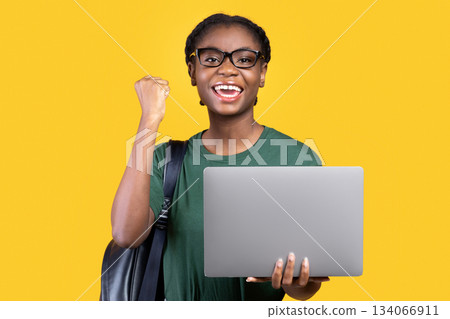 Joyful Black Female Student With Laptop Gesturing Yes After Successful Online Exam Standing Posing On Yellow Studio Background. Joy Of E-Learning, Educational Gadgets, Distant Study Concept Joyful Black Female Student With Laptop Gesturing Yes After Successful Online Exam Standing Posing On Yellow Studio Background. Joy Of E-Learning, Educational Gadgets, Distant Study Concept 134066911