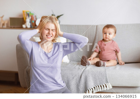 Postnatal depression concept. Stressed blonde woman young mother suffering from headache, sitting with baby at home, touching her head and screaming. Motherhood, multi-tasking and family Postnatal depression concept. Stressed blonde woman young mother suffering from headache, sitting with baby at home, touching her head and screaming. Motherhood, multi-tasking and family 134066915