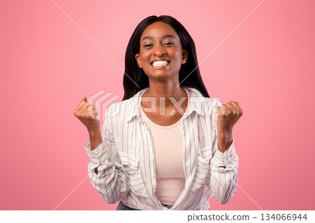 Emotional black woman gesturing YES on pink studio background. Pretty African American lady celebrating success with clenched fists, feeling excited or triumphant Emotional black woman gesturing YES on pink studio background. Pretty African American lady celebrating success with clenched fists, feeling excited or triumphant 134066944
