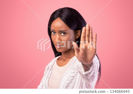 Young black woman gesturing STOP on pink studio background. Displeased African American lady saying NO, showing rejection gesture, expressing her negative attitude 134066945