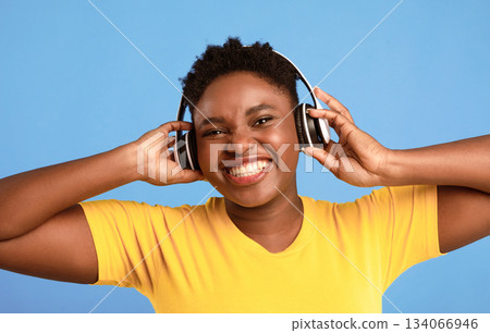 Positive Oversized Black Woman Wearing Wireless Headphones Listening To Music Smiling To Camera Posing Over Blue Studio Background. Great Playlist, Electronics, Music Lover Concept 134066946