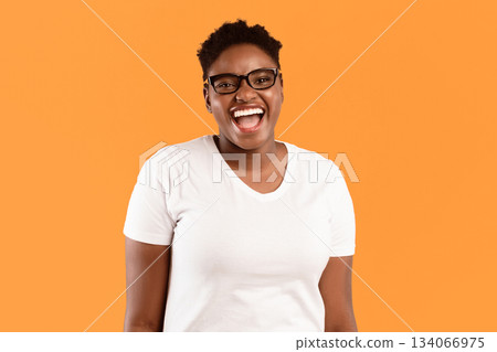 Happy Plus-Size African American Woman's Portrait. Cheerful Black Lady Smiling To Camera Posing Standing In Studio Over Yellow Background, Wearing Eyeglasses. Positive Emotions Concept Happy Plus-Size African American Woman's Portrait. Cheerful Black Lady Smiling To Camera Posing Standing In Studio Over Yellow Background, Wearing Eyeglasses. Positive Emotions Concept 134066975