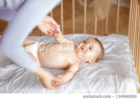 Good morning sunshine. Smiling little baby laying in cot, holding mom's hands, ready to wake up. Top view of cute blonde toddler waking up, lying in wooden baby bed, grabbing mother fingers Good morning sunshine. Smiling little baby laying in cot, holding mom's hands, ready to wake up. Top view of cute blonde toddler waking up, lying in wooden baby bed, grabbing mother fingers 134066989