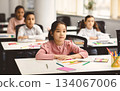 Return Back To School. Portrait of focused diligent asian female pupil sitting with folded arms at desk with group of diverse classmates, listening to teacher, selective focus. Academic Concept 134067006